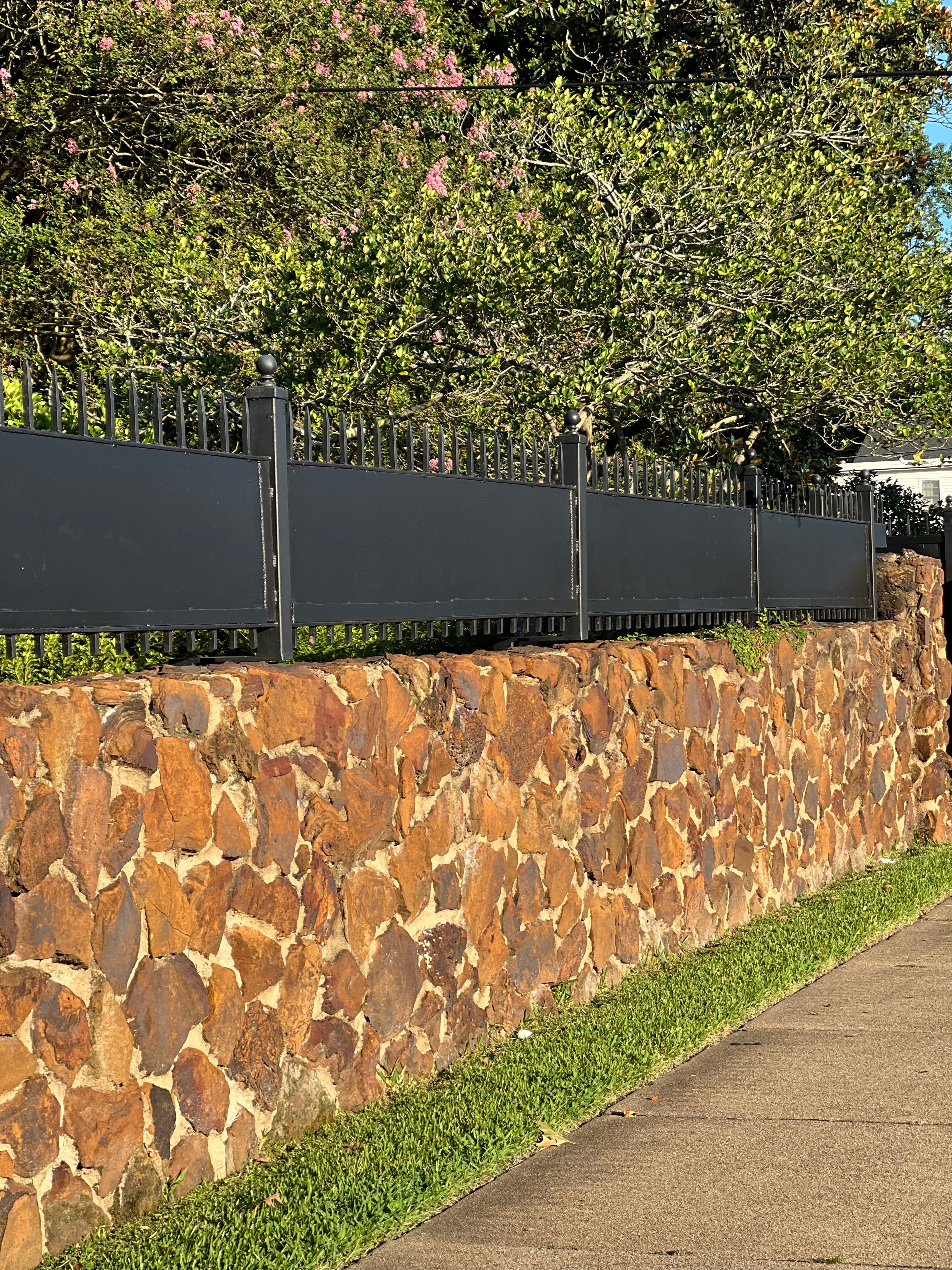 Black steel louvered privacy fence panels installed atop stone retaining wall with crepe myrtle — Fortified Fence and Weld, Alexandria LA