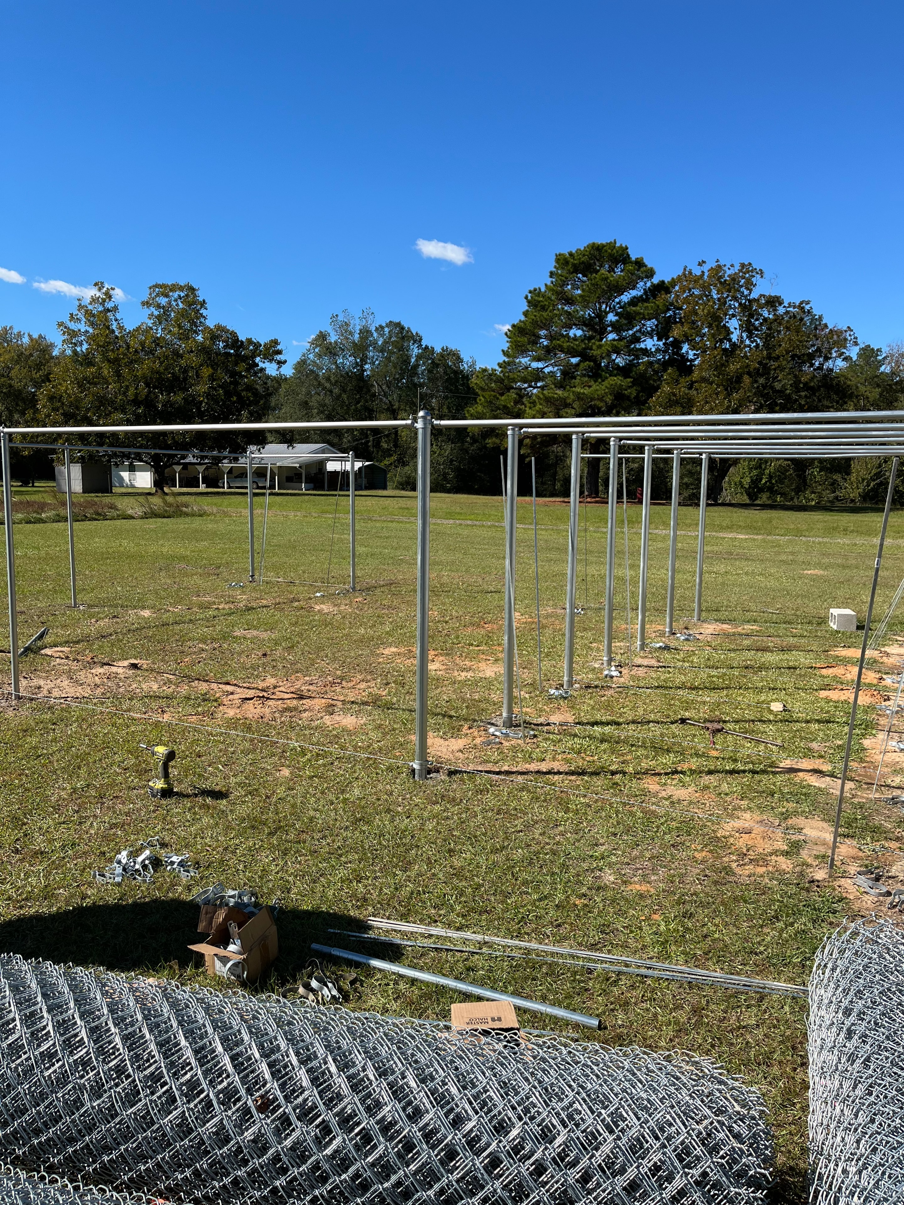 Galvanized chain link fence posts set and staged in open field with chain link rolls ready for installation — Fortified Fence and Weld, Central Louisiana