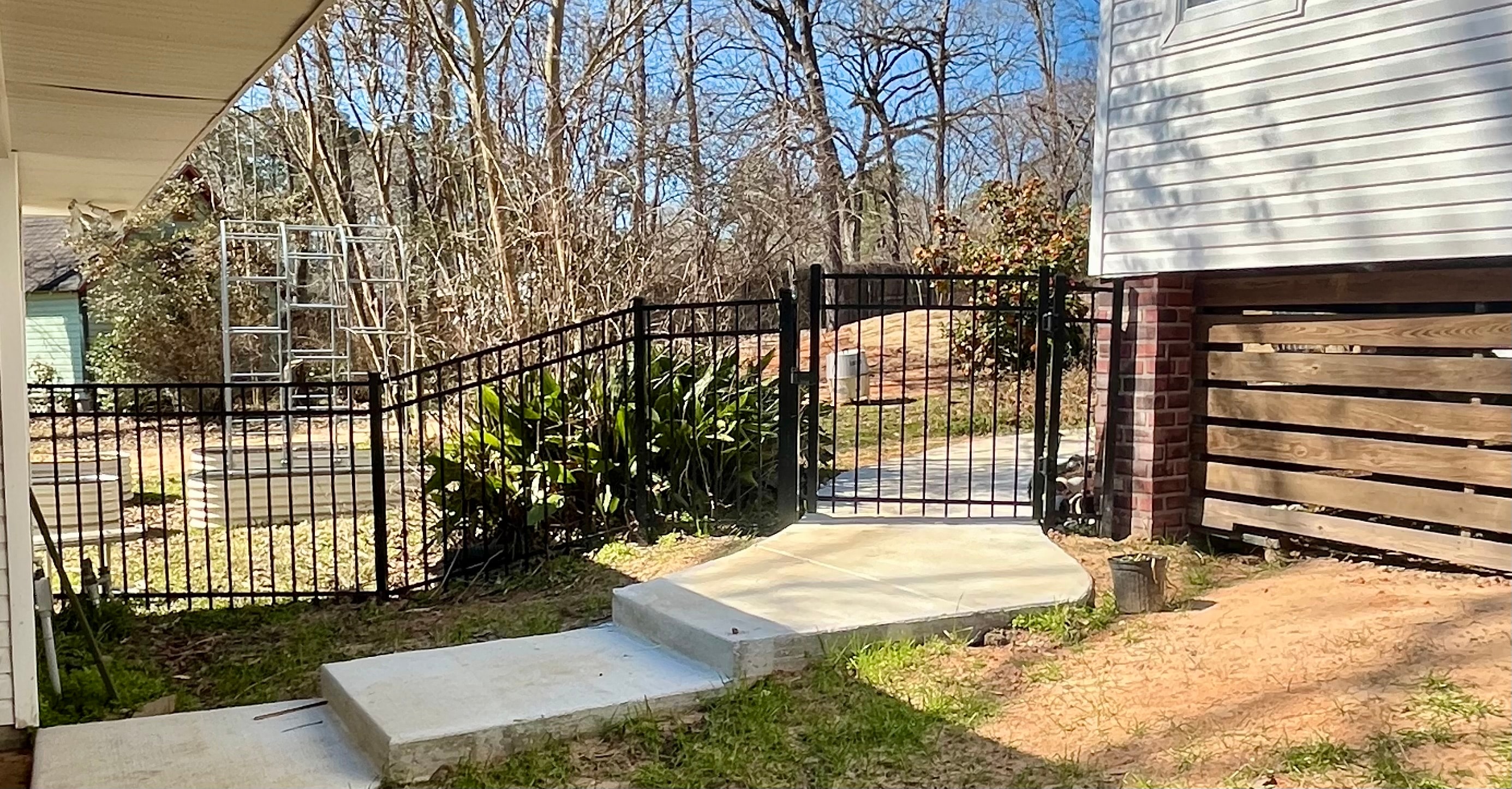 Black ornamental aluminum fence with arched swing gate on concrete pad beside brick column and wood horizontal fence panel — Fortified Fence and Weld, Alexandria LA