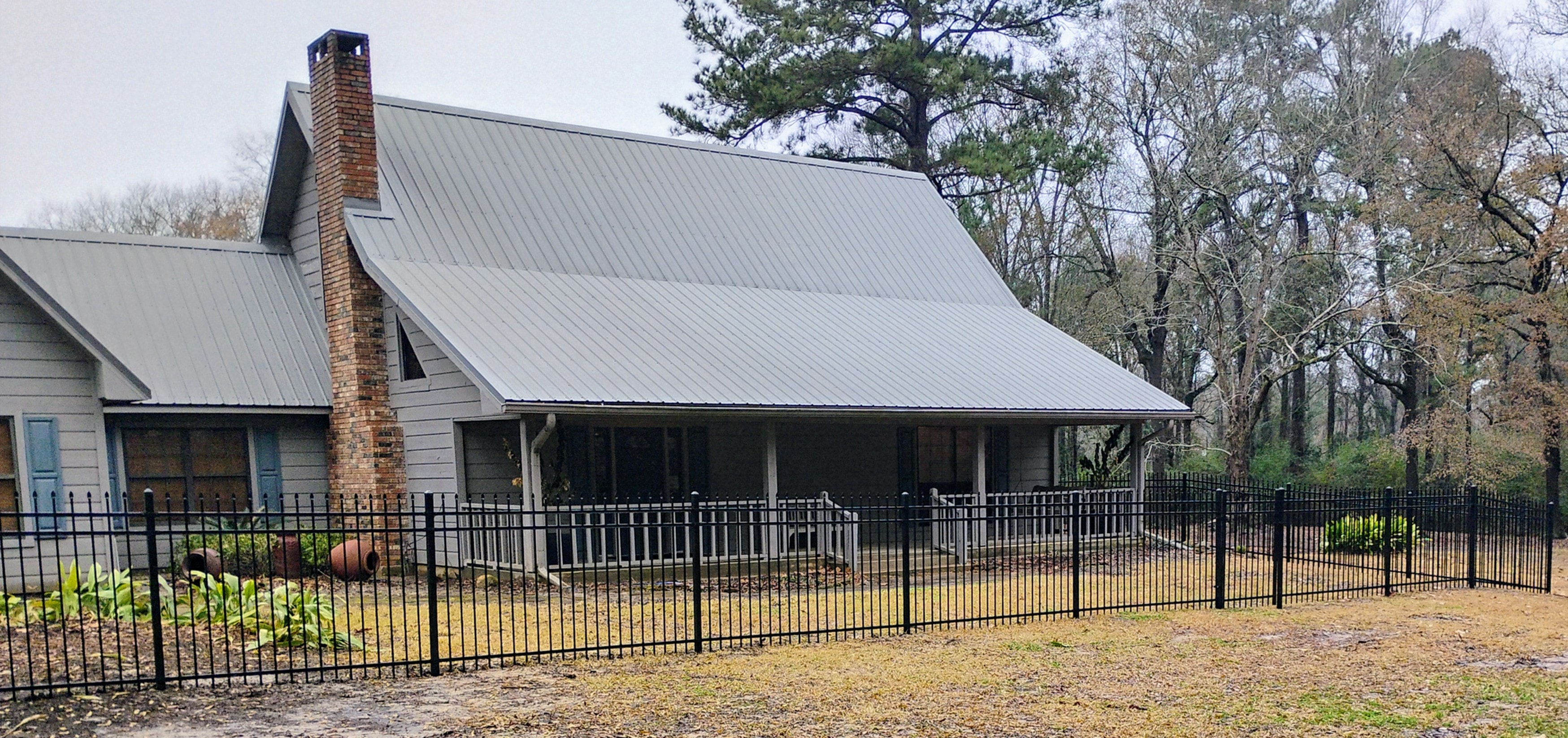 Black ornamental iron fence surrounding farmhouse with metal roof in Central Louisiana – Fortified Fence and Weld