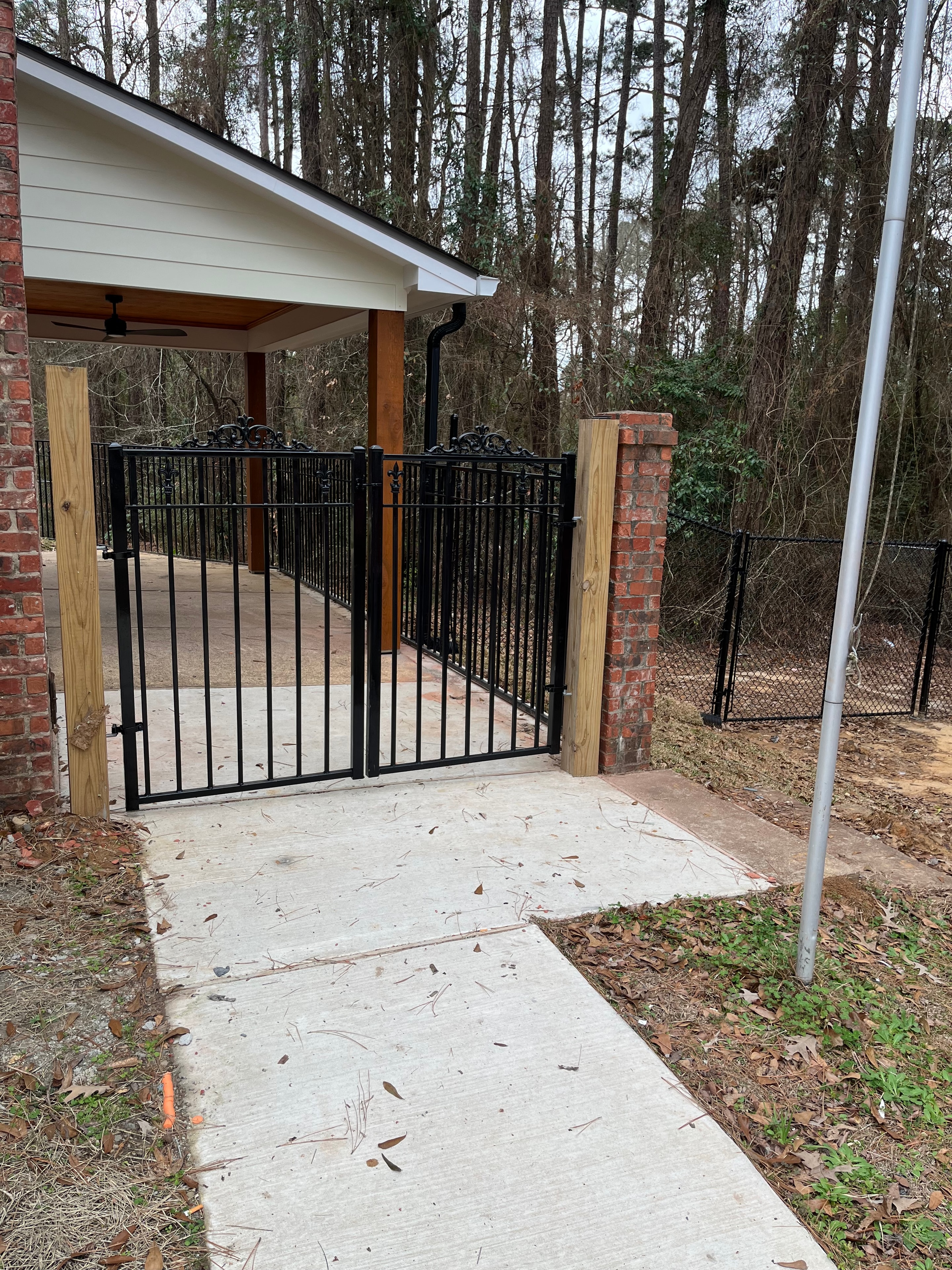 Custom black ornamental iron double swing gate with scroll details, wider view showing full gate and brick surround — Fortified Fence and Weld, Alexandria LA