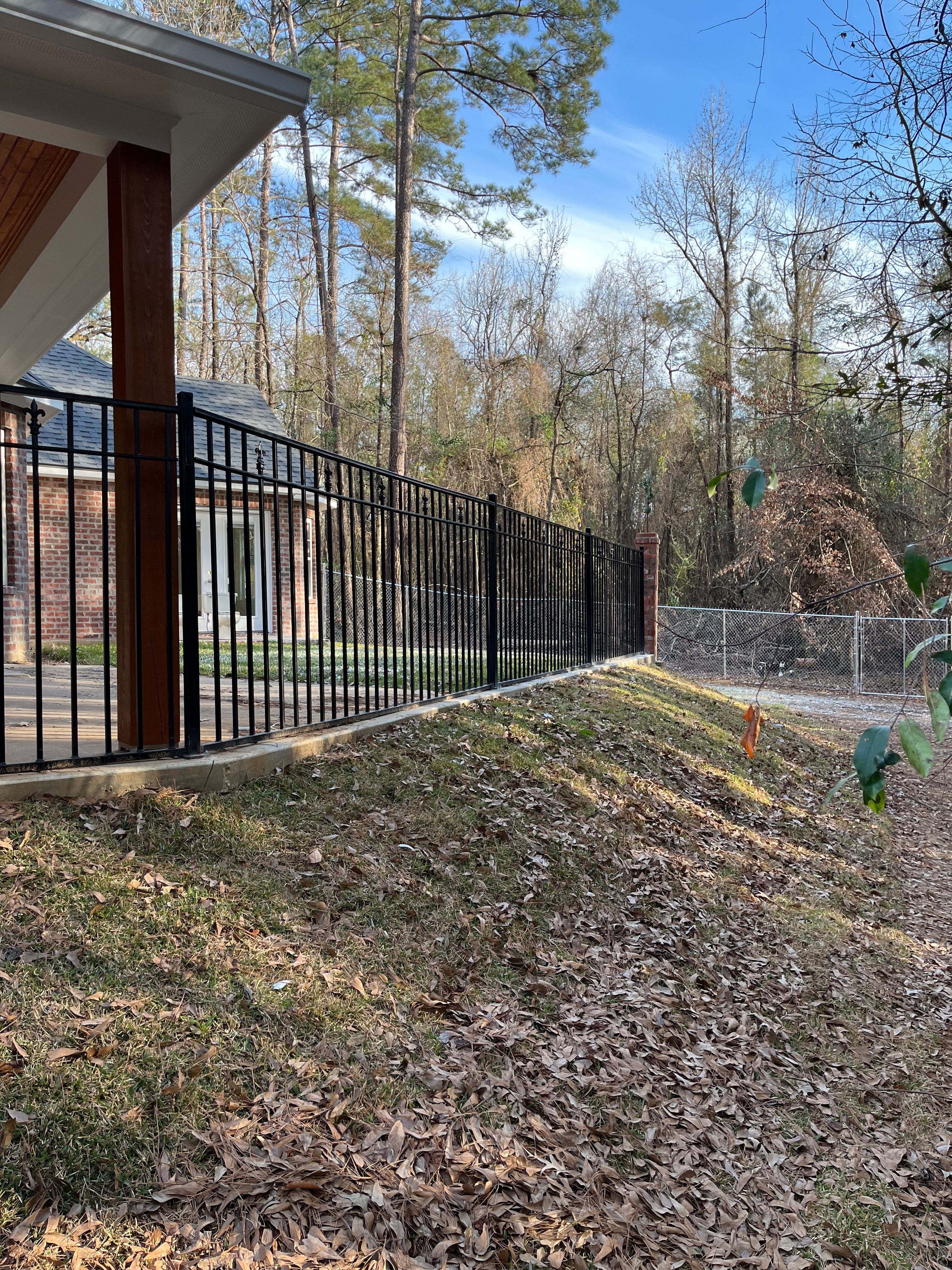 Long black steel horizontal slat fence and railing running along brick retaining wall with chain link fence behind — Fortified Fence and Weld, Alexandria LA
