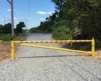 Yellow powder-coated swing arm barrier gate installed on gravel road in Central Louisiana – Fortified Fence and Weld