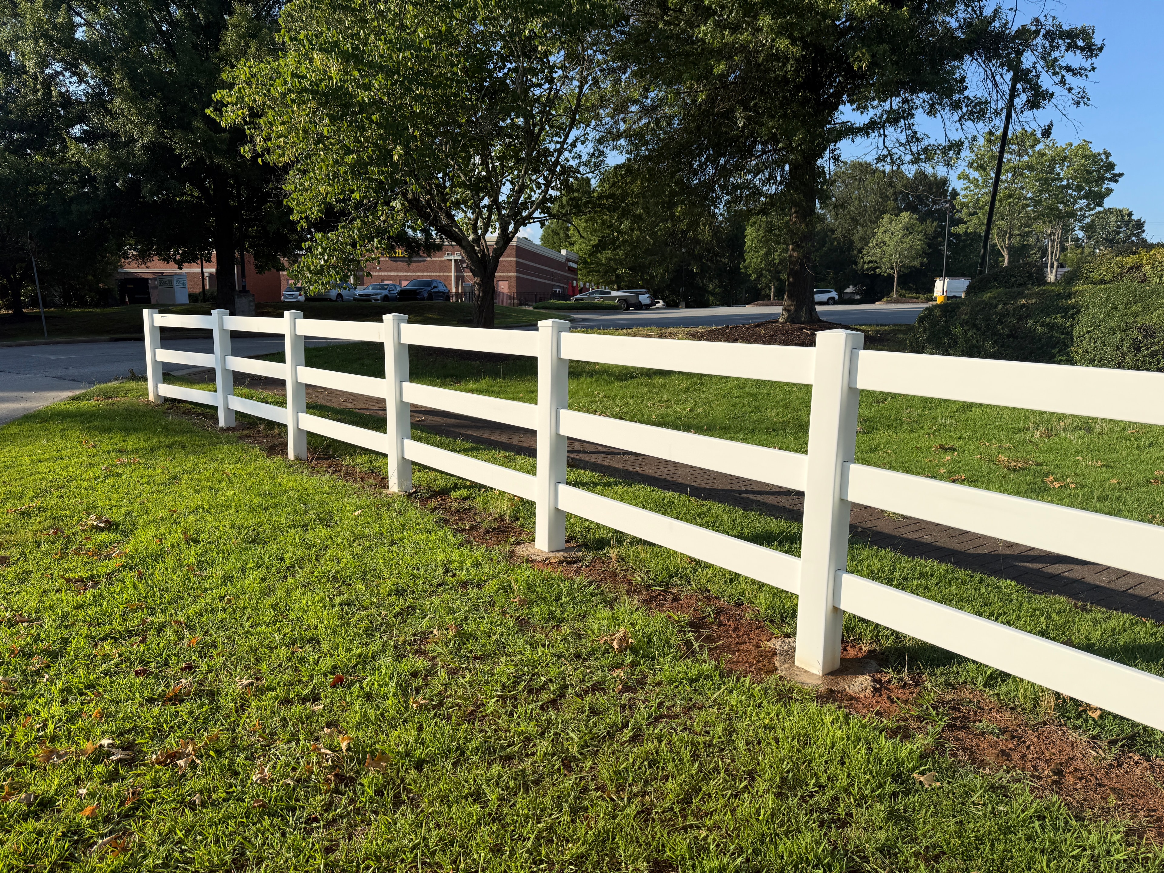 White vinyl 3-rail fence close-up with red clay soil and brick walkway — Fortified Fence and Weld, Alexandria LA