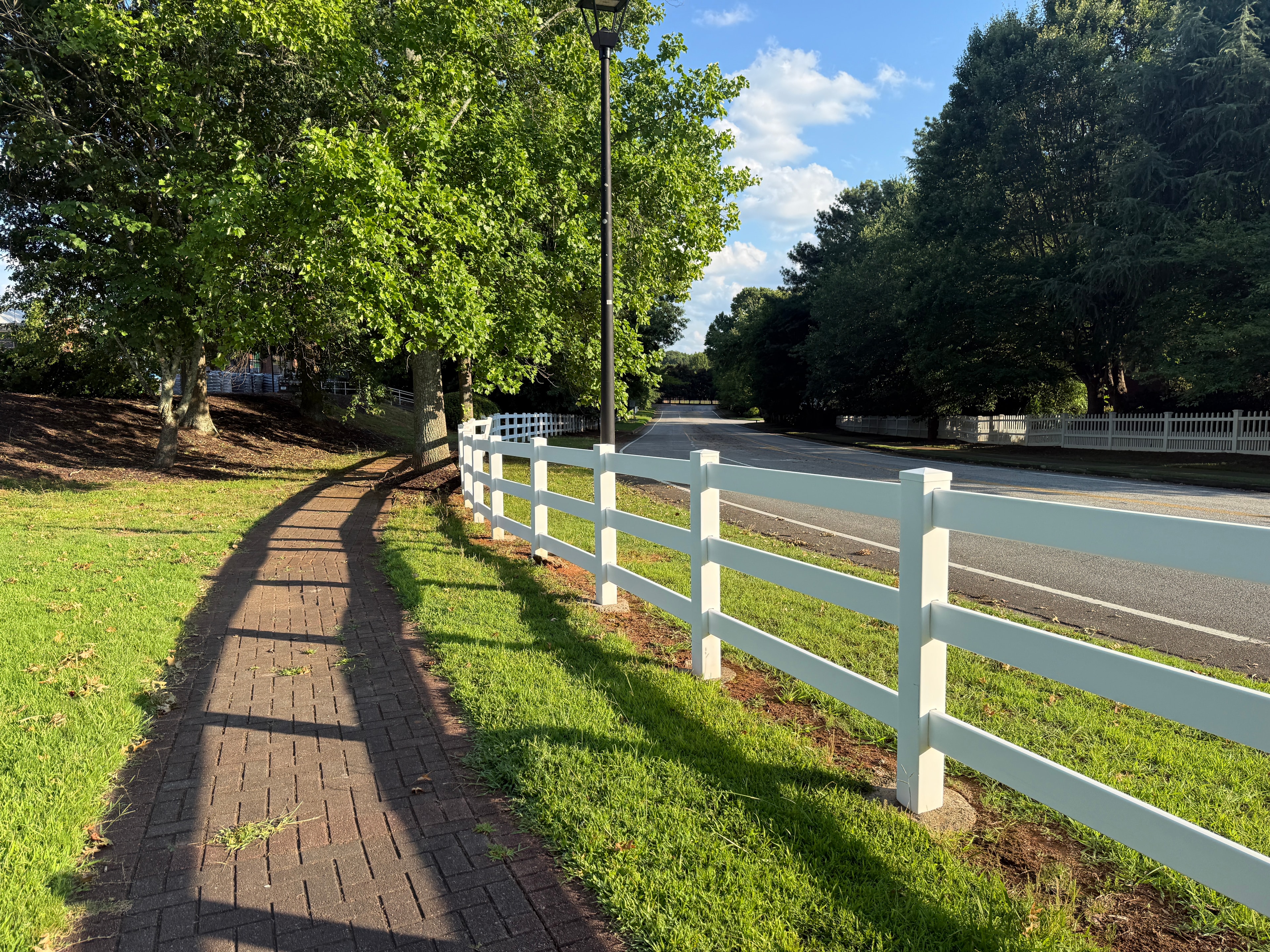 White vinyl 3-rail fence running along tree-lined brick driveway pathway — Fortified Fence and Weld, Alexandria LA