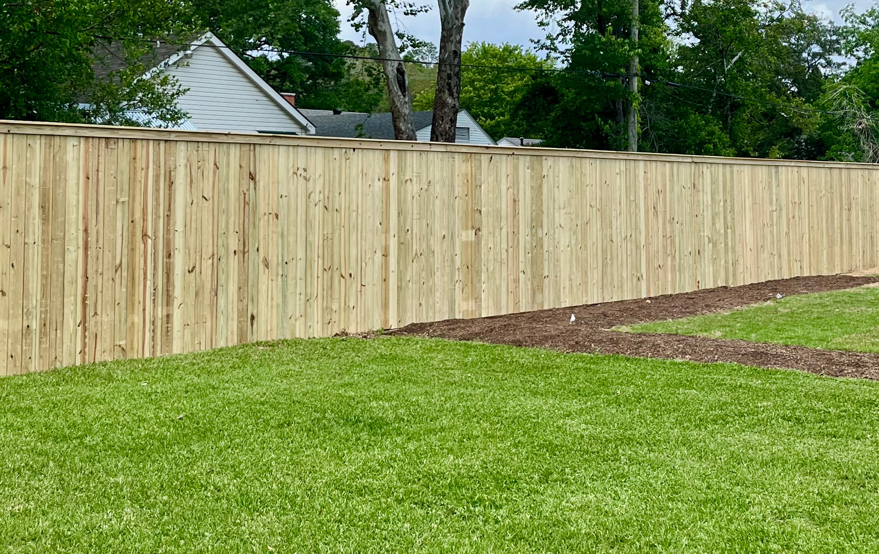 Fresh cedar wood privacy fence installed along residential backyard with green lawn in Central Louisiana — Fortified Fence and Weld